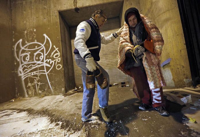 Doctor Angelo hands over the shoes off his feet to help a homeless man under the overpasses on Lower Wacker Drive in Chicago
