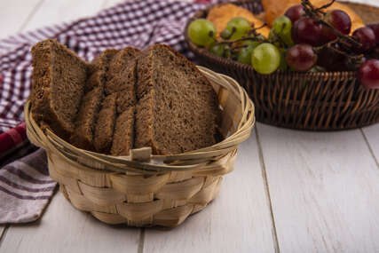side view of rye bread slices in basket on plaid cloth with basket of grapes nectacots on wooden background
