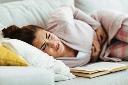 Young woman with stomachache lying down on sofa in the living room.